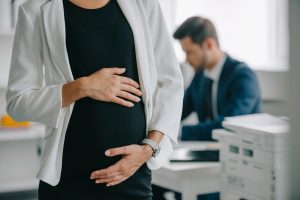 partial view of pregnant businesswoman and colleague at workplace in office