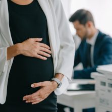 partial view of pregnant businesswoman and colleague at workplace in office